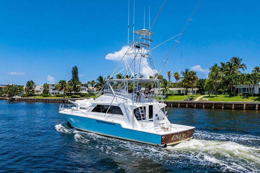 1998 Bertram 60 Convertible yacht cruising on a sunny day, surrounded by palm trees.