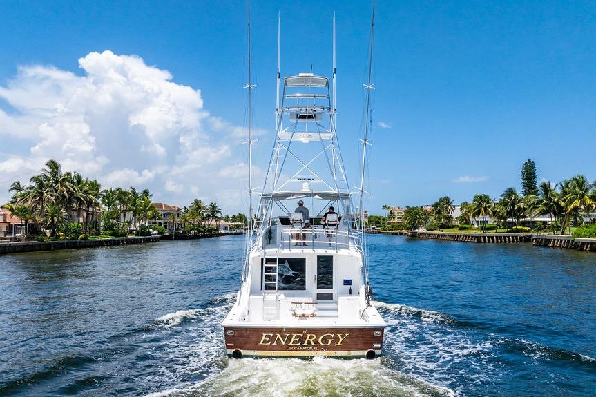 1998 Bertram 60 Convertible yacht cruising on a sunny waterway, surrounded by palm trees.