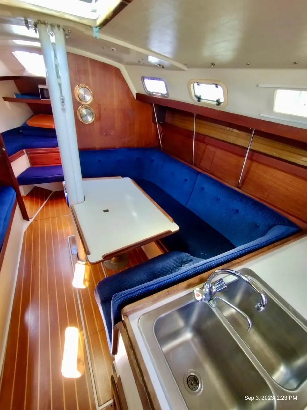 Interior of a 1987 Catalina 34 yacht with blue upholstery and wooden flooring.