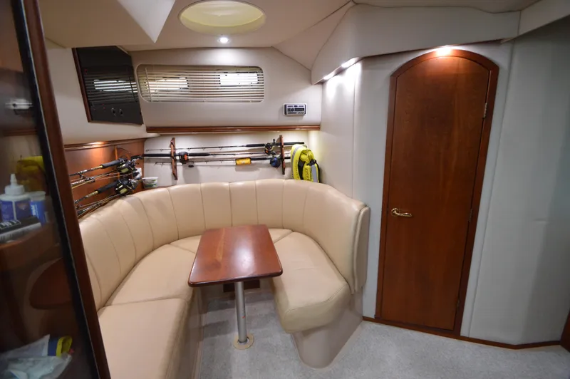 Side Chick Yacht Photos Pics 2002 Rampage 38 Express cabin with beige seating, wooden table, and fishing rods.