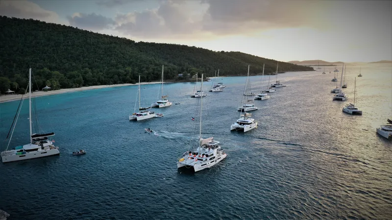 Barefeet Retreat Yacht Photos Pics Aerial view of multiple catamarans, including a 2020 Royal Cape Catamarans Majestic 570, anchored near a lush coastline.