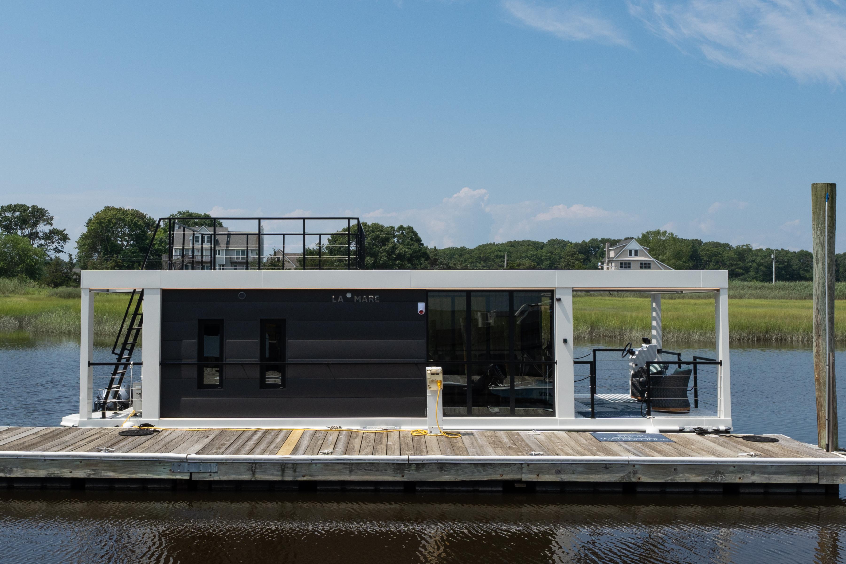 Modern Waterlodge 11 houseboat docked on a serene river, showcasing sleek design and rooftop deck.