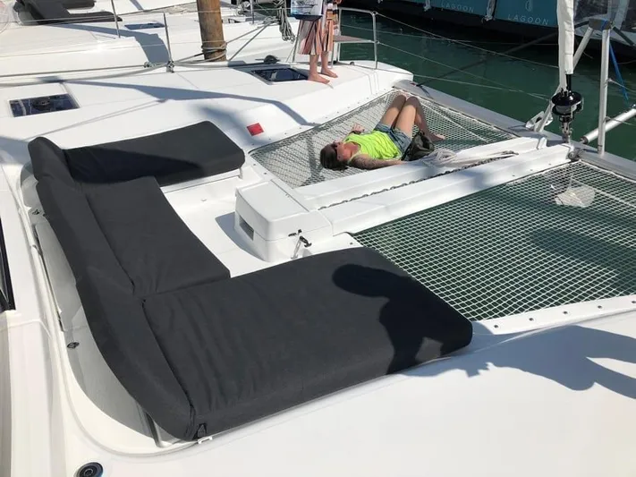 Clearlake III Yacht Photos Pics Person relaxing on Lagoon 46 catamaran's netted deck, 2021 model, in sunny marina.