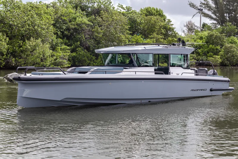  Yacht Photos Pics 2024 Axopar 37XC CROSS CABIN boat on calm water, surrounded by lush greenery.