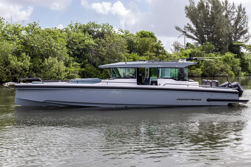  Yacht Photos Pics 2024 Axopar 37XC CROSS CABIN boat on calm water, surrounded by lush greenery.