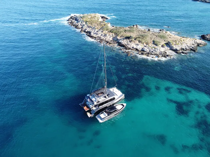 Full Moon Yacht Photos Pics Aerial view of 2024 Moon 60 Sail yacht near rocky island in clear blue waters.