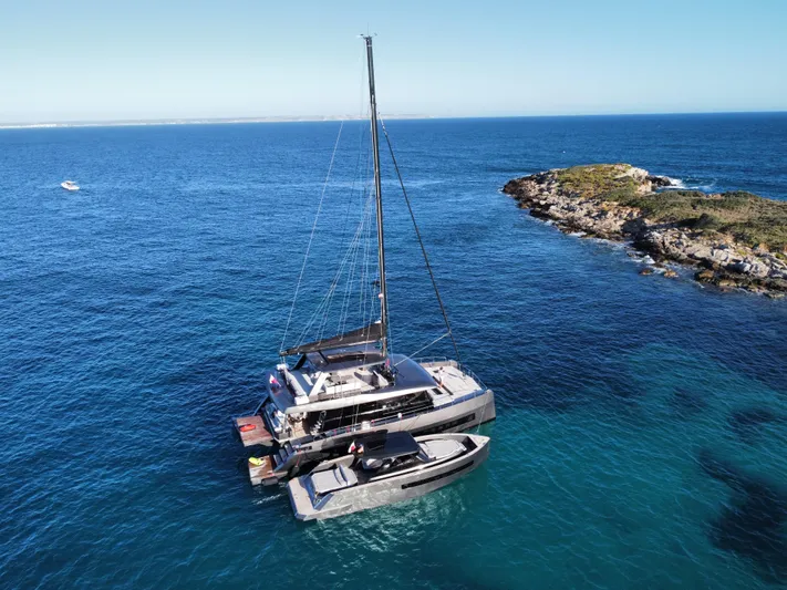 Full Moon Yacht Photos Pics 2024 Moon 60 Sail catamaran anchored near rocky island in clear blue ocean.