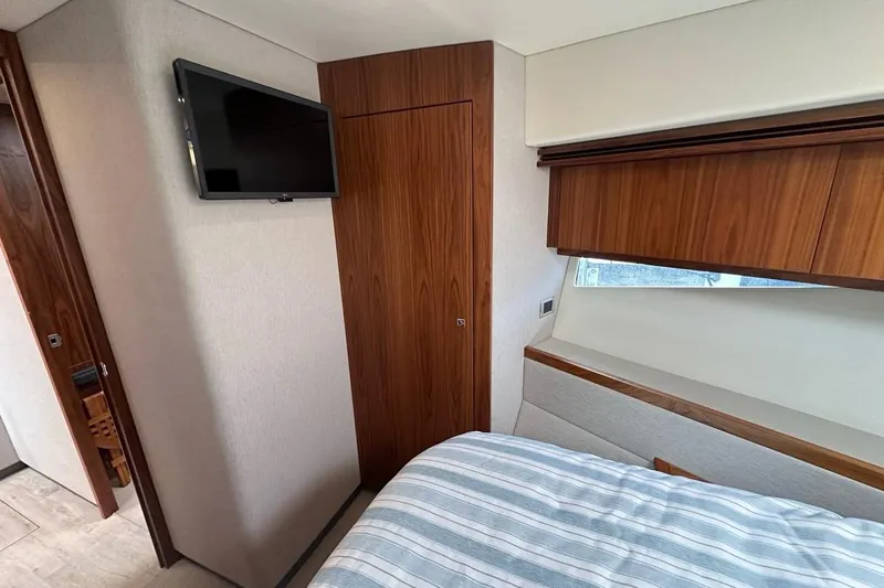 Happy Ours Yacht Photos Pics 2019 Riviera 5400 Sport Yacht bedroom with TV, wooden accents, and striped bedding.