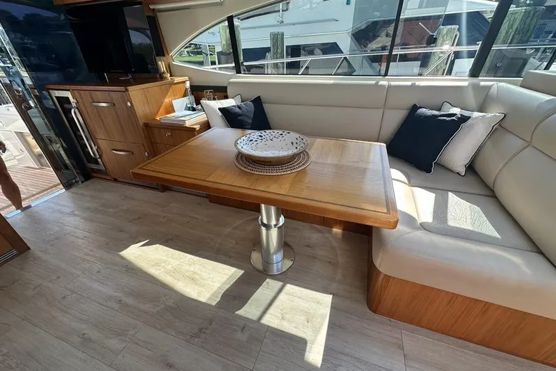 Happy Ours Yacht Photos Pics Interior of 2019 Riviera 5400 Sport Yacht with wooden table and plush seating.