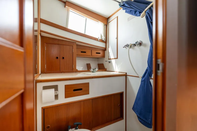 Celebration Yacht Photos Pics 1988 Grand Banks 42 Classic yacht bathroom with wooden cabinetry and blue shower curtain.