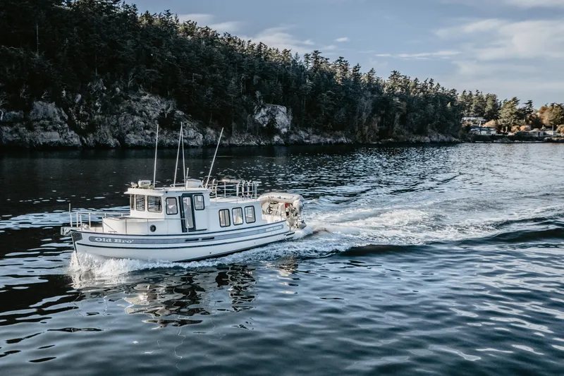 Old Bro Yacht Photos Pics 2001 Nordic Tug 32 cruising on a serene lake with forested shoreline.