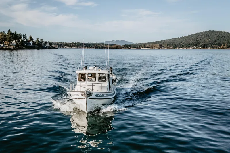 Old Bro Yacht Photos Pics 2001 Nordic Tug 32 cruising on a serene lake with forested hills in the background.