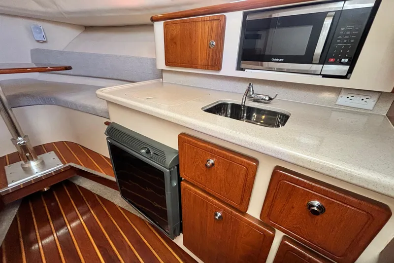  Yacht Photos Pics 2006 Pursuit 3070 Offshore boat interior with kitchenette, featuring sink, microwave, and seating area.