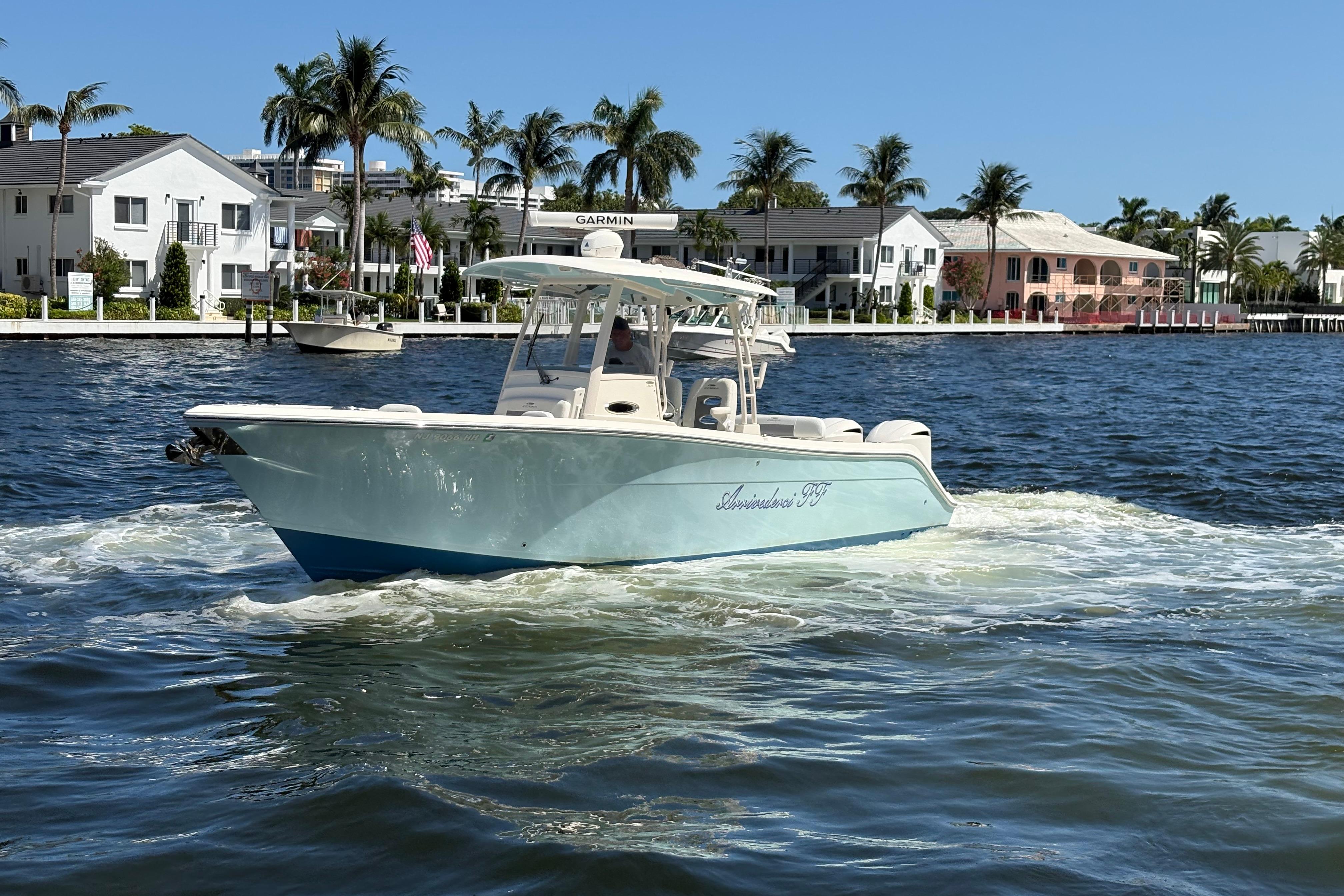 2018 Cobia 301 Center Console boat cruising on a sunny waterfront with palm trees.