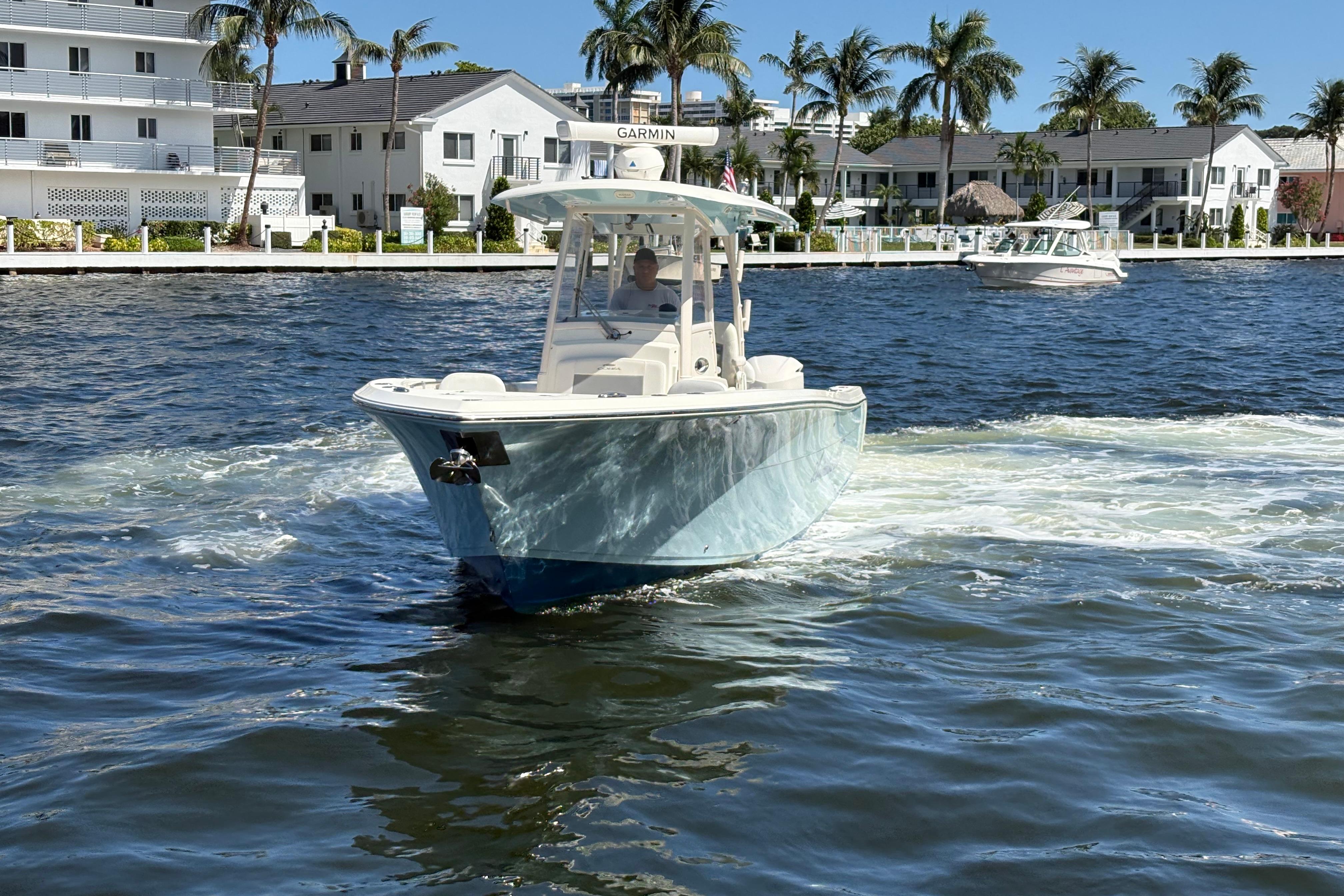 2018 Cobia 301 Center Console boat cruising on a sunny waterfront with palm trees.
