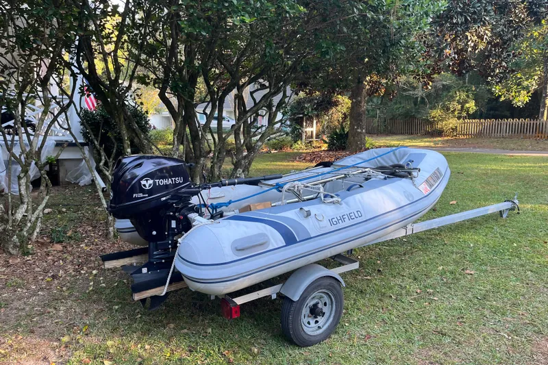 Moon Howler Yacht Photos Pics Inflatable boat with Tohatsu motor on trailer, parked on grass near trees.