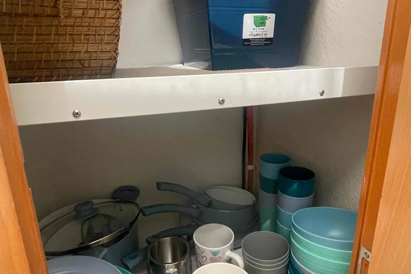 Endless Summer Yacht Photos Pics Kitchen pantry with cookware, mugs, and stacked bowls on shelves.