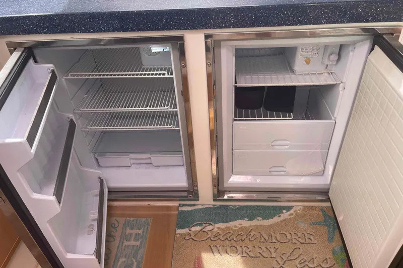 Endless Summer Yacht Photos Pics Open Admiral Executive 2008 refrigerator with empty shelves and drawers, on a beach-themed rug.