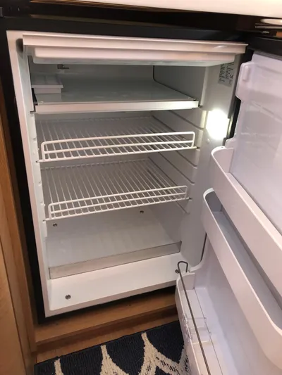  Yacht Photos Pics Empty refrigerator inside 2024 Jeanneau Sun Odyssey 440 yacht, featuring wire shelves and door storage.