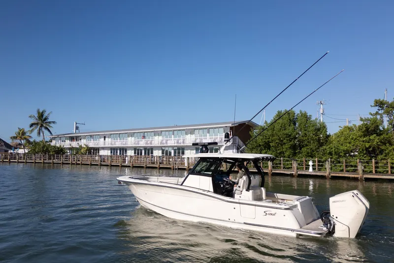 Natural 9 Yacht Photos Pics 2024 Scout 330 LXF boat cruising near waterfront building under clear blue sky.