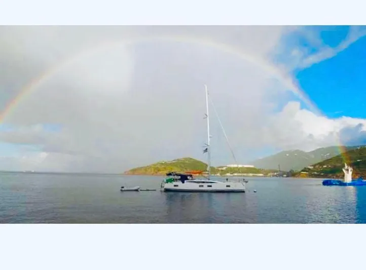 Caretta2 Yacht Photos Pics Sailboat Jeanneau 54 (2018) anchored under a rainbow in a serene bay.