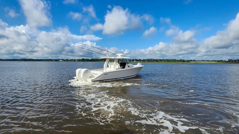 Blown Dough Yacht Photos Pics 2023 Pursuit S 358 Sport boat cruising on a calm, scenic waterway under a blue sky.