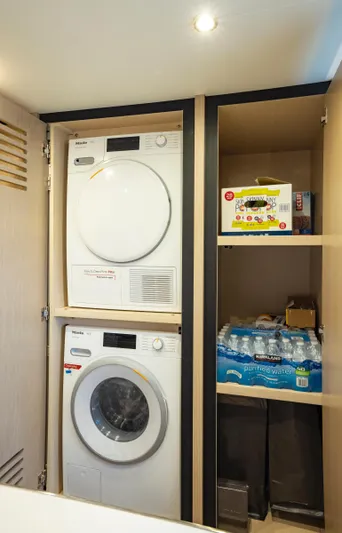 Aquila 70 Yacht Photos Pics Laundry area with stacked washer and dryer, storage shelves, and bottled water in Aquila 70 Luxury yacht.