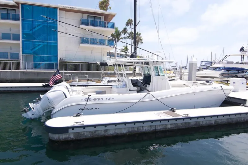  Yacht Photos Pics 2023 World Cat 325 CC boat docked at marina, with American flag and modern building backdrop.