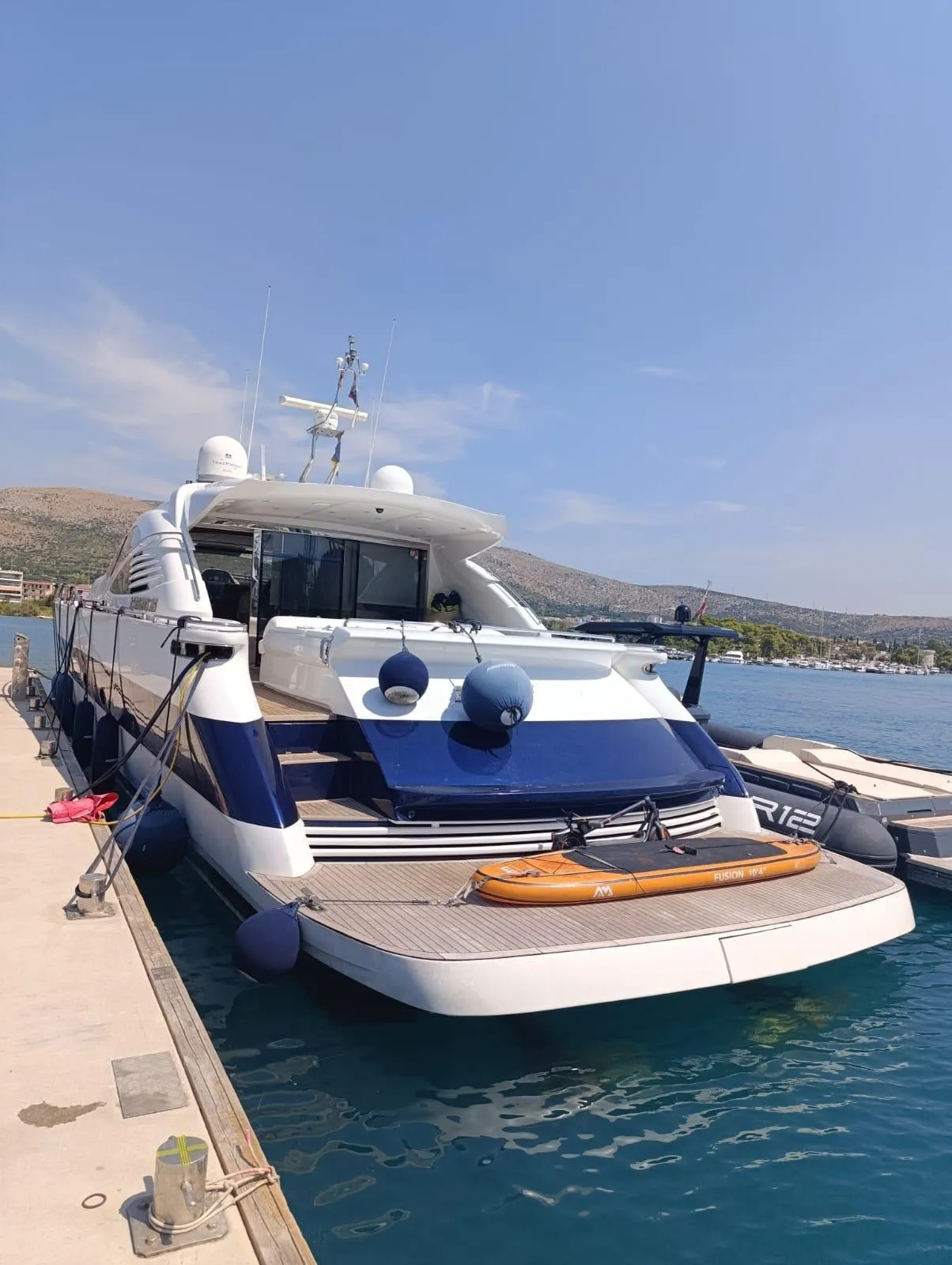 Luxury 2005 Pershing 76 yacht docked at marina under clear blue sky.