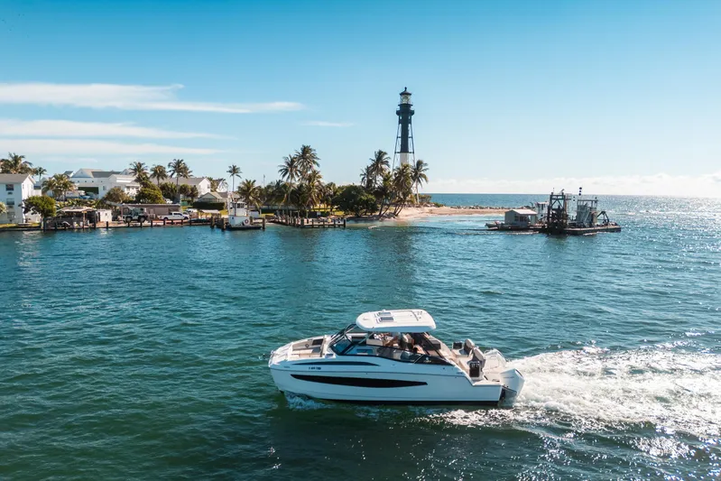 Era Ora Yacht Photos Pics Aquila 32 Sport 2022 cruising near a lighthouse and palm-lined shore.