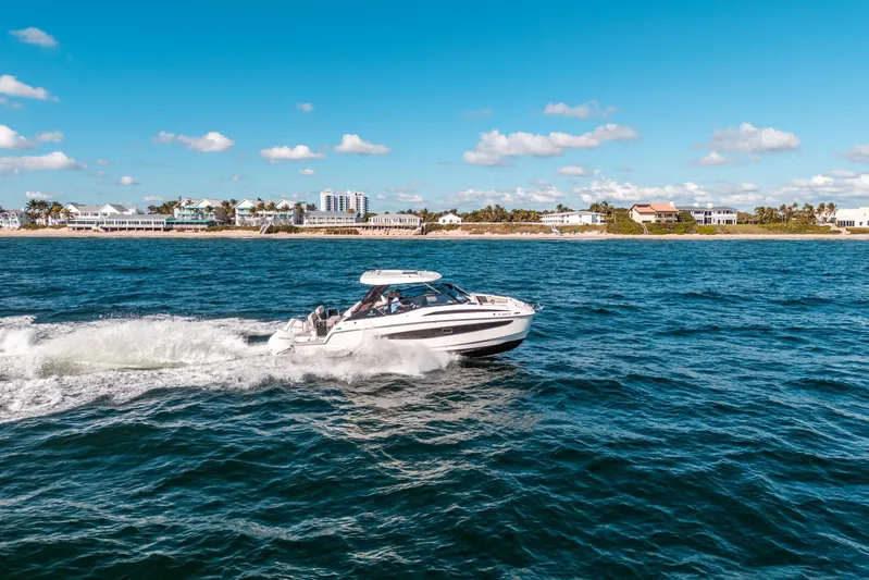 Era Ora Yacht Photos Pics Aquila 32 Sport 2022 cruising on ocean near coastal homes under blue sky.