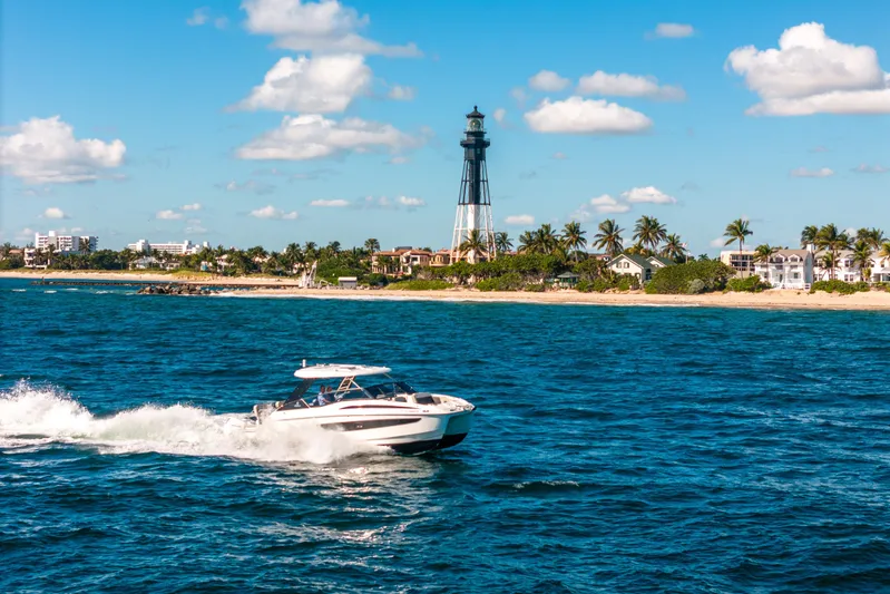 Era Ora Yacht Photos Pics Aquila 32 Sport 2022 cruising near a coastal lighthouse under a clear blue sky.