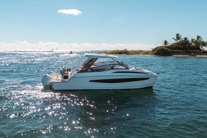 Era Ora Yacht Photos Pics Aquila 32 Sport 2022 boat cruising on sunny, tropical waters near a lush island.