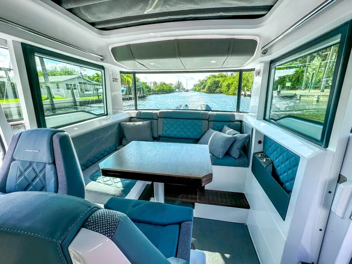  Yacht Photos Pics 2024 Axopar 37XC CROSS CABIN interior with seating and table, featuring large windows and modern design.