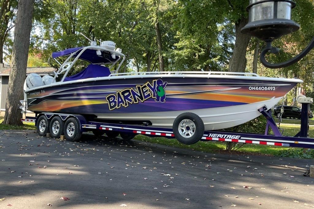 2014 Concept Boats 36CC on trailer, vibrant "Barney" design, parked in wooded area.