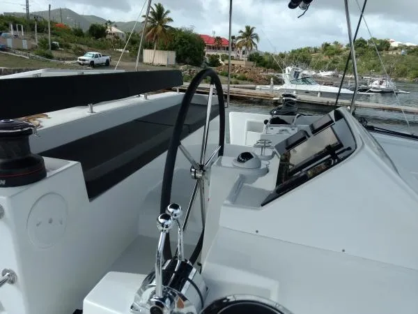 Smooth Sailor Yacht Photos Pics 2019 Lagoon 450 catamaran helm with steering wheel, docked in a tropical marina setting.
