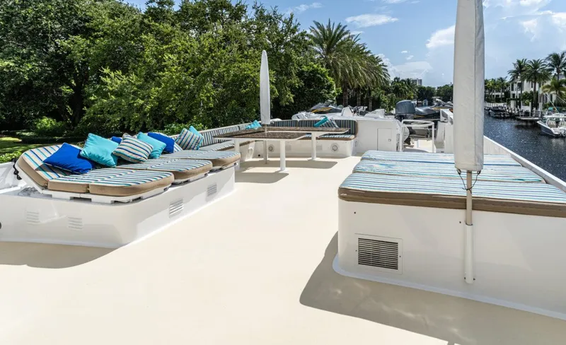 Le Montrachet Yacht Photos Pics 1986 Broward Flybridge yacht deck with striped cushions and lush greenery.