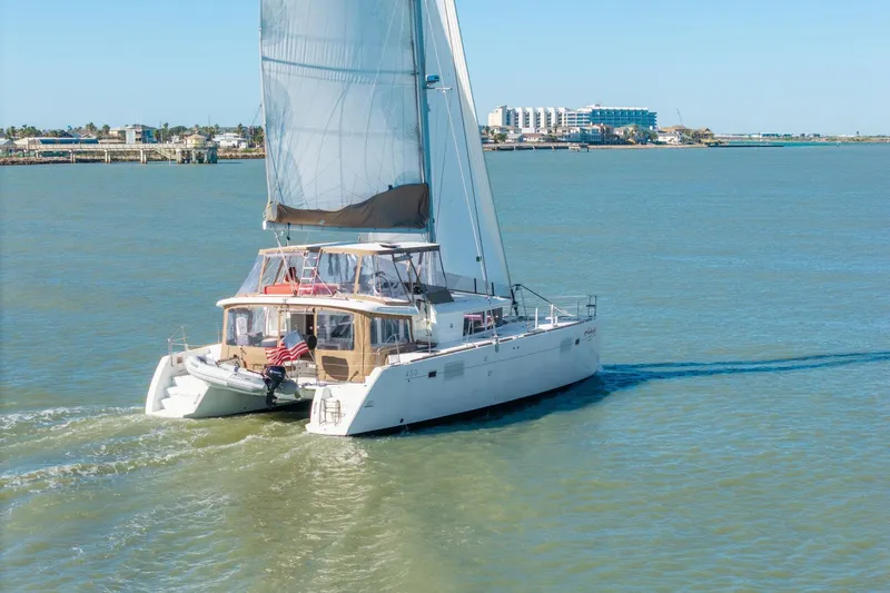 Audacity Yacht Photos Pics 2013 Lagoon 450 catamaran sailing on calm waters near coastal buildings.