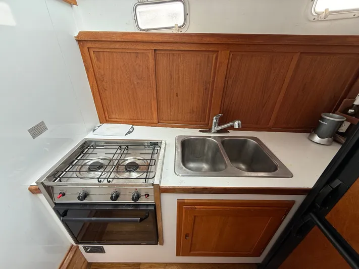 Screamer Yacht Photos Pics Compact kitchen in 1998 Wilbur 38 Downeast boat with stove, sink, and wooden cabinetry.