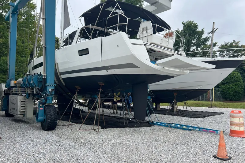  Yacht Photos Pics 2023 Jeanneau 65 yacht on dry dock, supported by stands, with trees in the background.