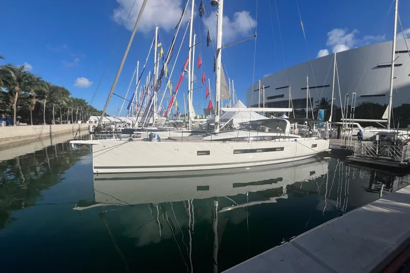  Yacht Photos Pics 2023 Jeanneau 65 yacht docked at marina, surrounded by flags and palm trees.