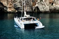 Catamaran NIMBLE 50, 2001 model, anchored in clear blue water near rocky cliffs.