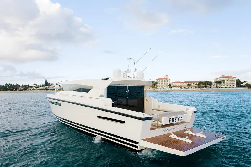 Freya Yacht Photos Pics 2023 Delta Powerboats 54 IPS cruising on clear blue waters near a coastal resort.