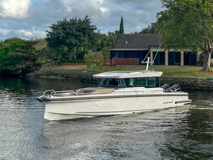  Yacht Photos Pics 2024 Axopar 37XC CROSS CABIN boat cruising on a calm river near a house.