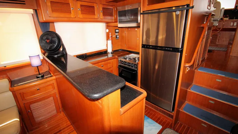 The Concession Yacht Photos Pics 2001 Selene 53 Pilothouse kitchen with wood cabinetry, stainless steel appliances, and black countertops.