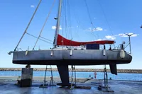 Sailboat "Finot Open 50" 2005 model on dry dock, with red sail, against blue sky.
