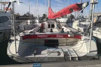 Finot Open 50 sailboat, 2005 model, docked at marina with red sail.