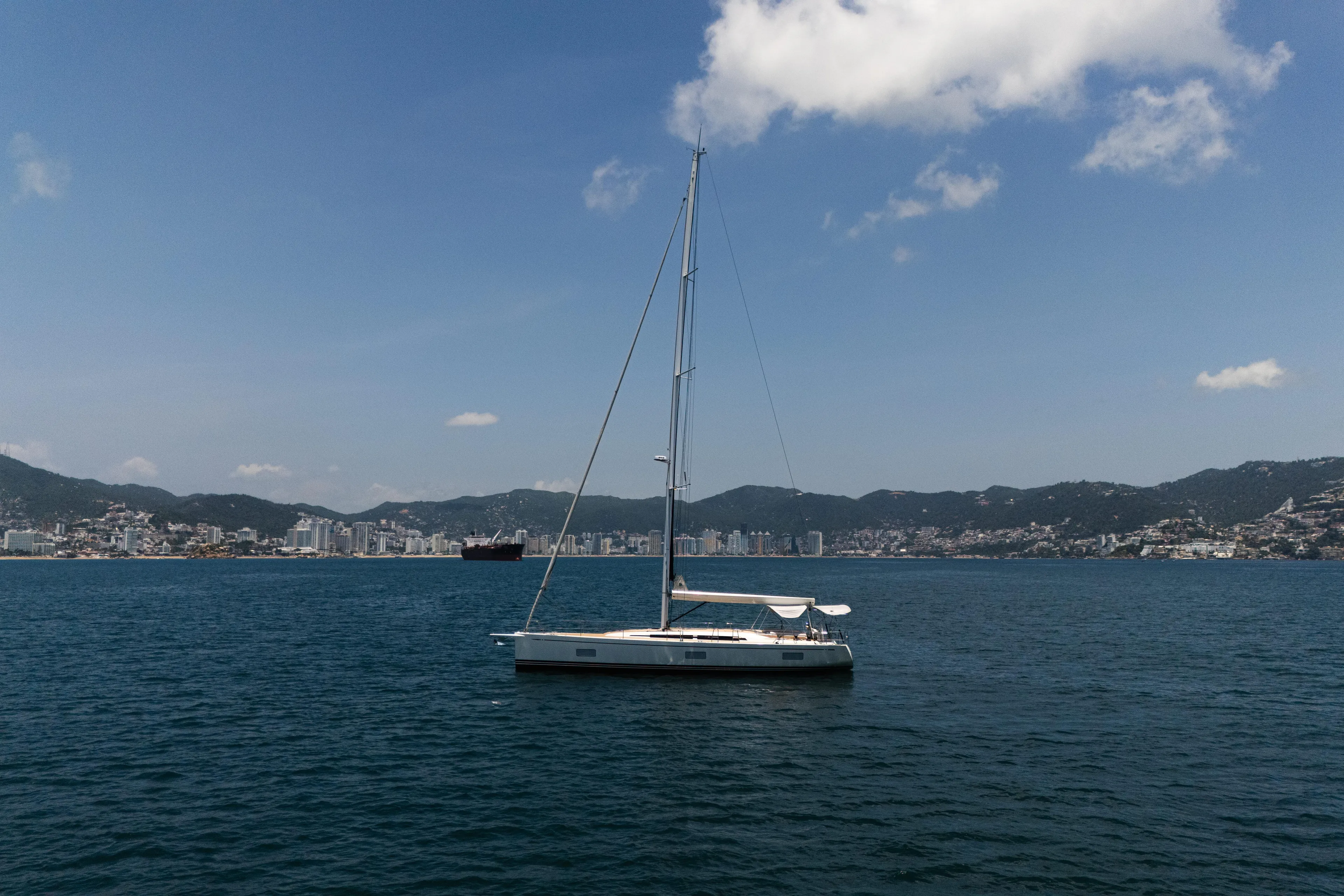 Invictus Yacht Photos Pics 2023 Nautor Swan 55 yacht sailing near coastal city skyline under clear blue sky.