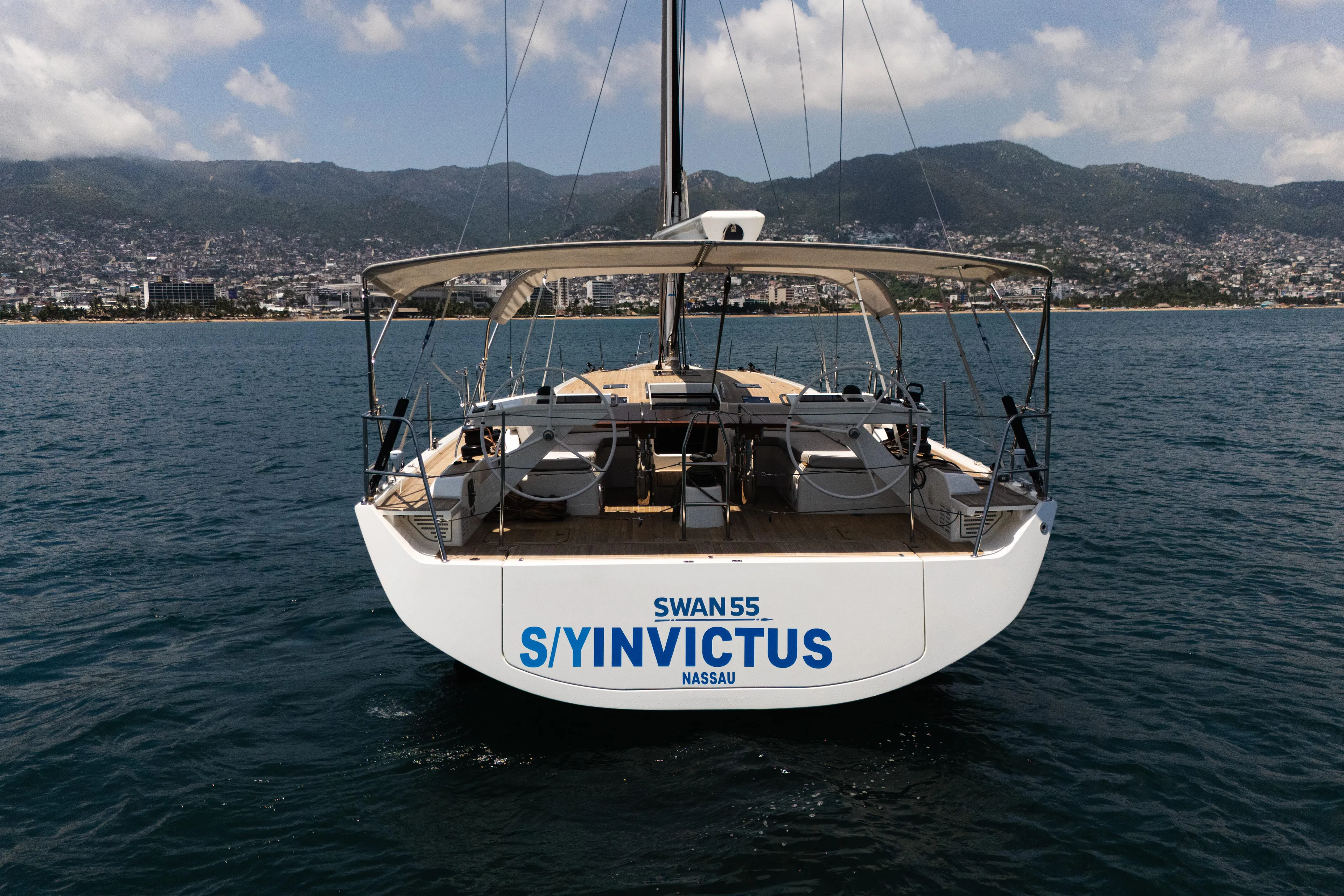 Invictus Yacht Photos Pics 2023 Nautor Swan 55 yacht "Invictus" on calm sea with coastal city backdrop.