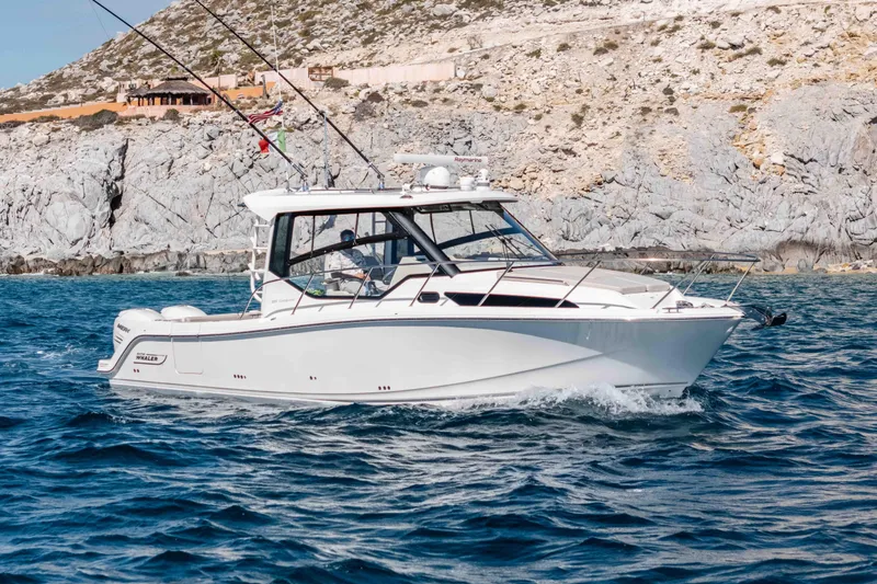 A Day In The Life Yacht Photos Pics 2021 Boston Whaler 325 Conquest boat cruising near rocky coastline.